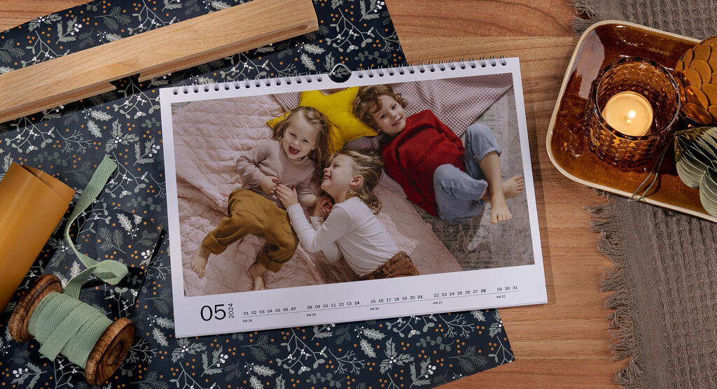 En fotokalender med et bilde av tre glade barn ligger på et bord, omgitt av innpakningspapir og bånd