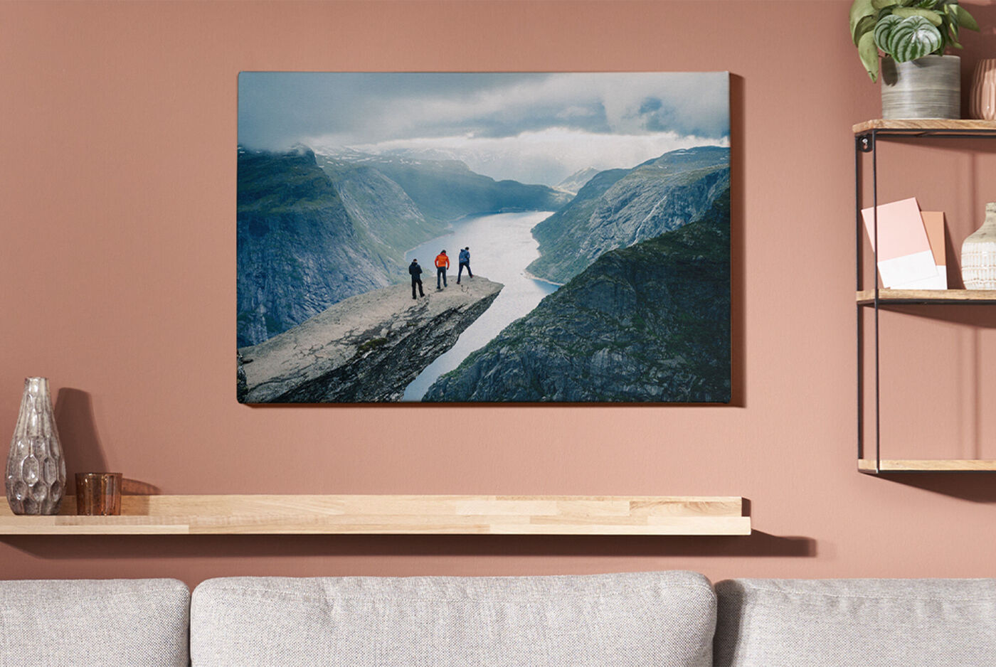 Tre personer står på en klippe og ser på en fjord med fjell i bakgrunnen.