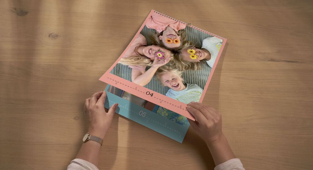 En person blar i en veggkalender med et bilde av smilende barn. Kalenderens sider er rosa og blå.