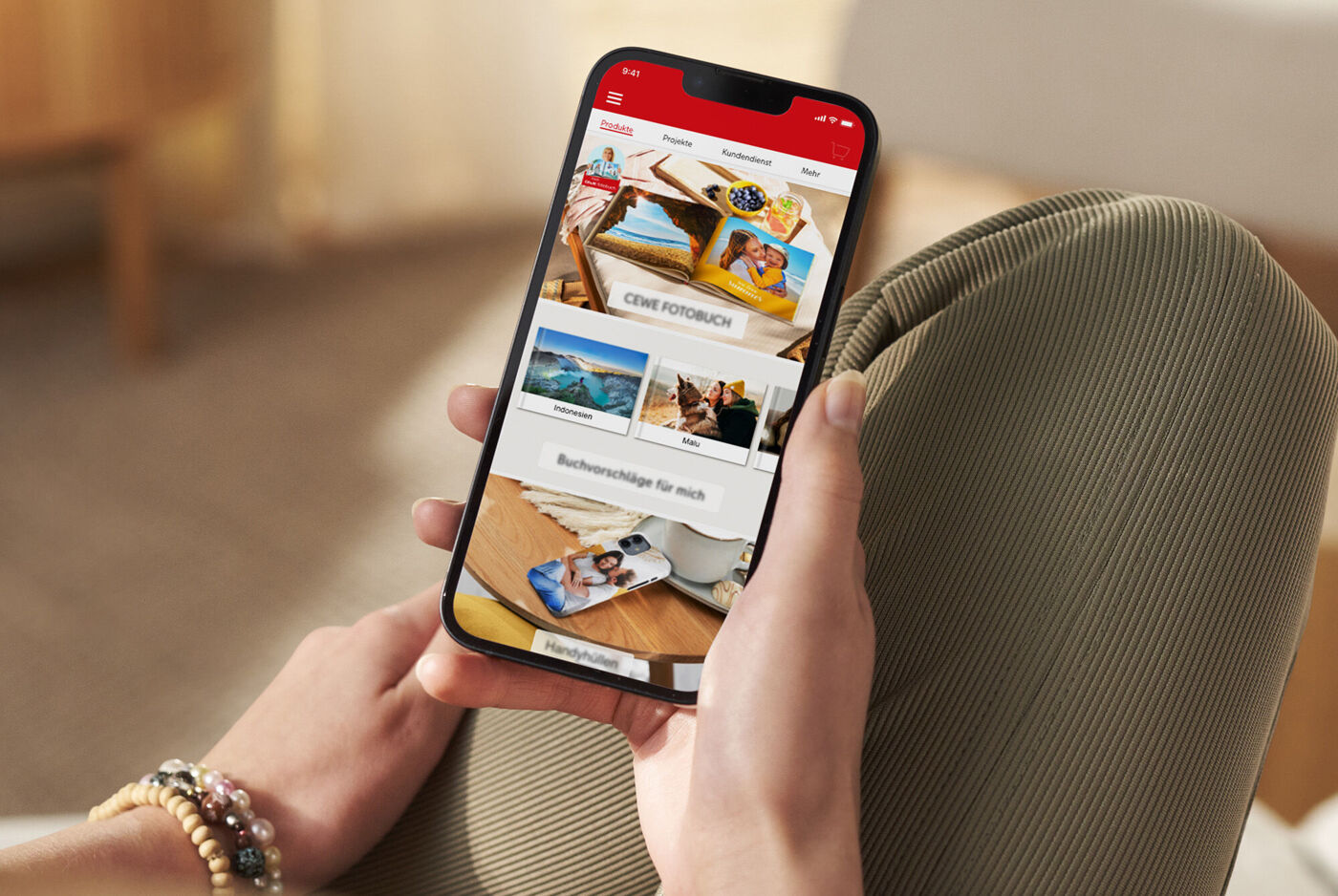 Person holder smarttelefon med CEWE-app, viser fotobøker